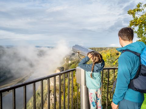 Ein Mädchen schaut durch ein Fernglas auf einer Aussichtsplattform in der Sächsischen Schweiz.