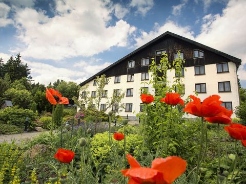 Das Hotel Forstmeister im Erzgebirge in der Außenansicht. Davor sind rote Blumen.