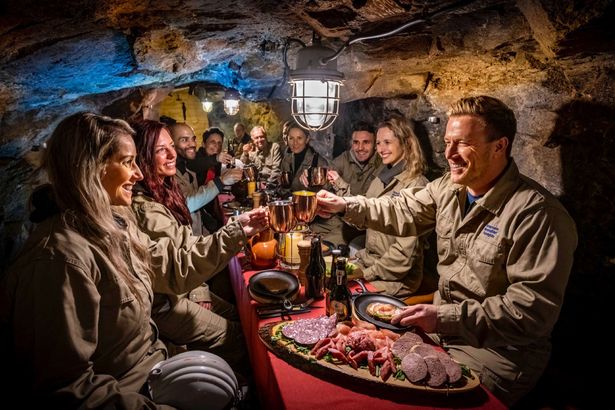 Eine Gruppe macht einen Bergmannsschmaus im Silberbergwerk Reiche Zeche in Freiberg. Sie haben eine Platte auf dem Tisch und stoßen miteinander an.