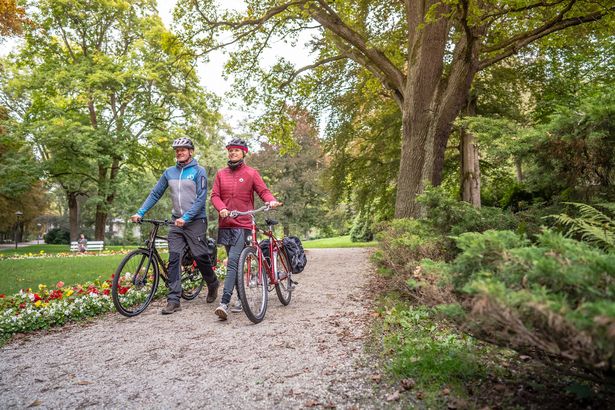 Eine Frau und ein Mann schieben ihr Fahrrad durch eine wunderschöne Parkanlage.