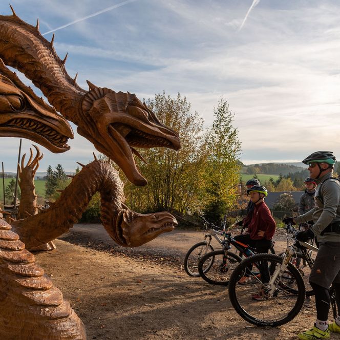 Eine Familie steht mit ihren Rädern am Rande der Blockline-Tour. Sie schauen auf Drachenfiguren aus Holz.