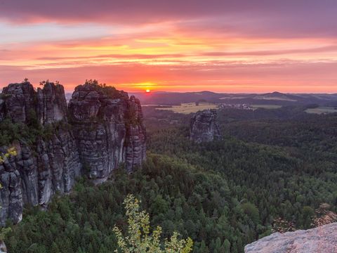 Links erheben sich die Schrammsteine im Nationalpark Sächsische Schweiz. Dahinter geht die Sonne unter.